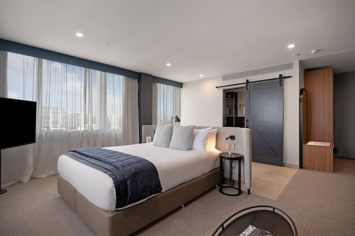 A modern hotel room with a large bed, a TV, a desk, and a sliding door.