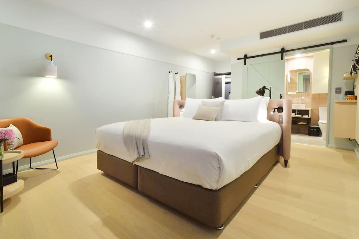 A modern bedroom with a large bed, a bedside table, a chair, and a mirror.
