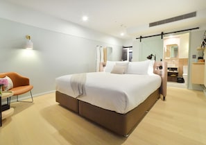 A modern bedroom with a large bed, a bedside table, a chair, and a mirror.