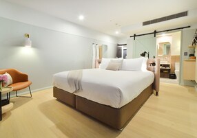 A modern bedroom with a large bed, a bedside table, a chair, and a mirror.