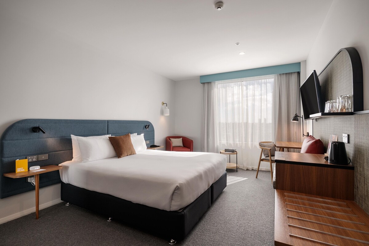 A modern hotel room with a large bed, a desk, a chair, and a television.