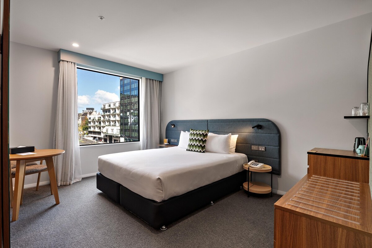A hotel room with a large bed, a desk, a chair, a telephone, and a coffee machine.