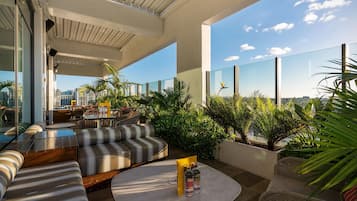 A rooftop terrace with outdoor seating, potted plants, and a clear view of the city skyline.