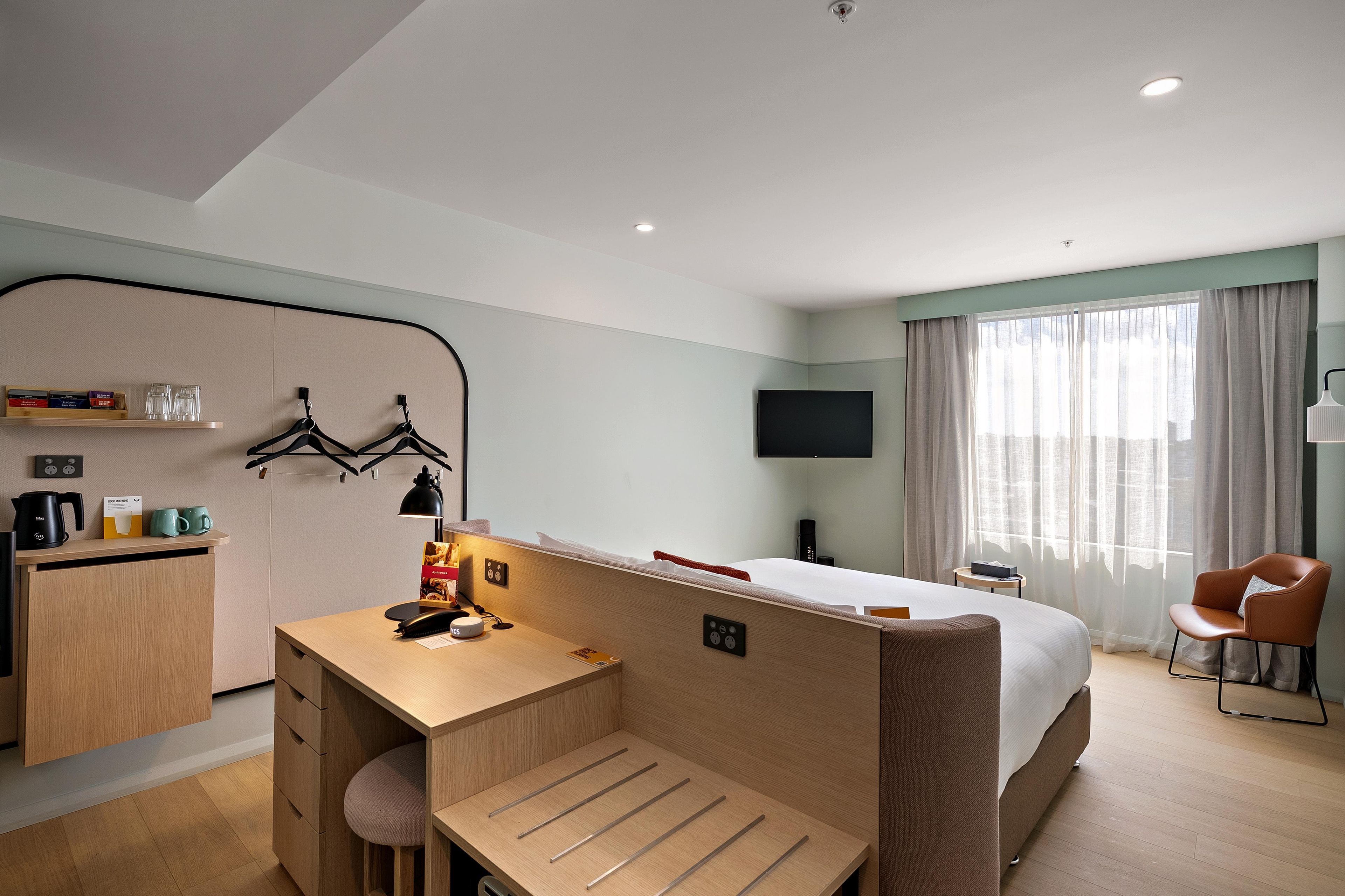 A hotel room with a bed, a desk with a chair, a television, and a window with curtains.