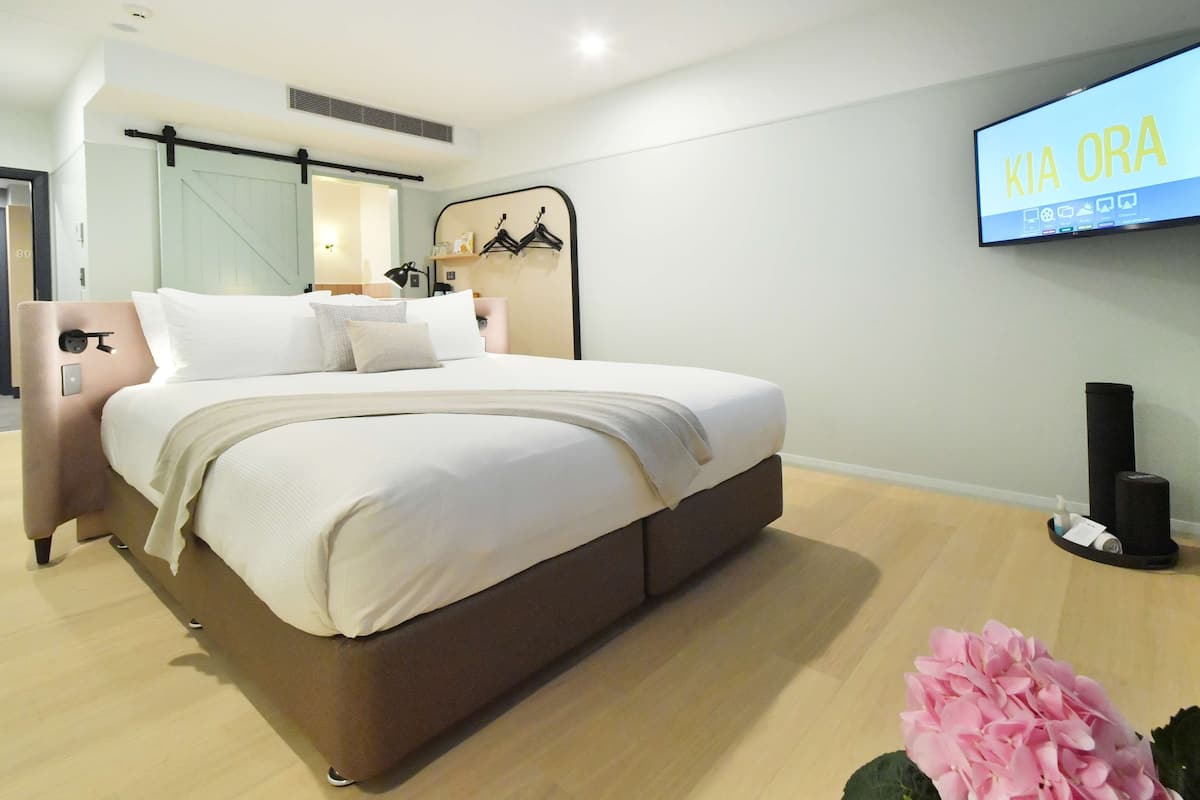 A modern hotel room with a large bed, a television mounted on the wall, and a sliding door closet.