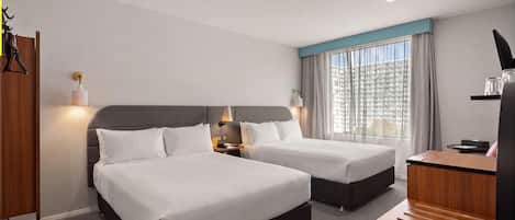 Habitación de hotel con dos camas, un escritorio, una silla y una ventana con cortinas.