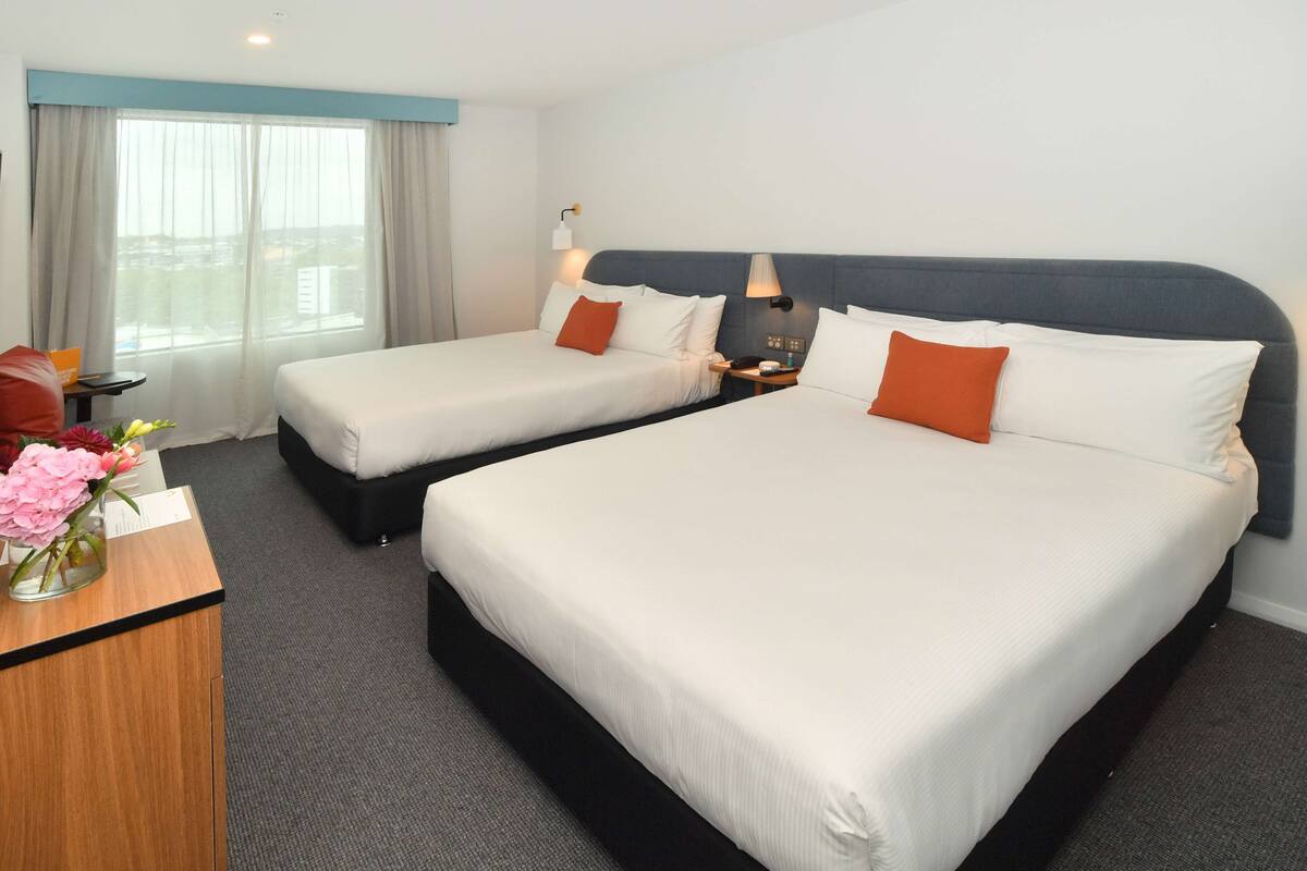 A hotel room with two beds, a desk, and a window with curtains.