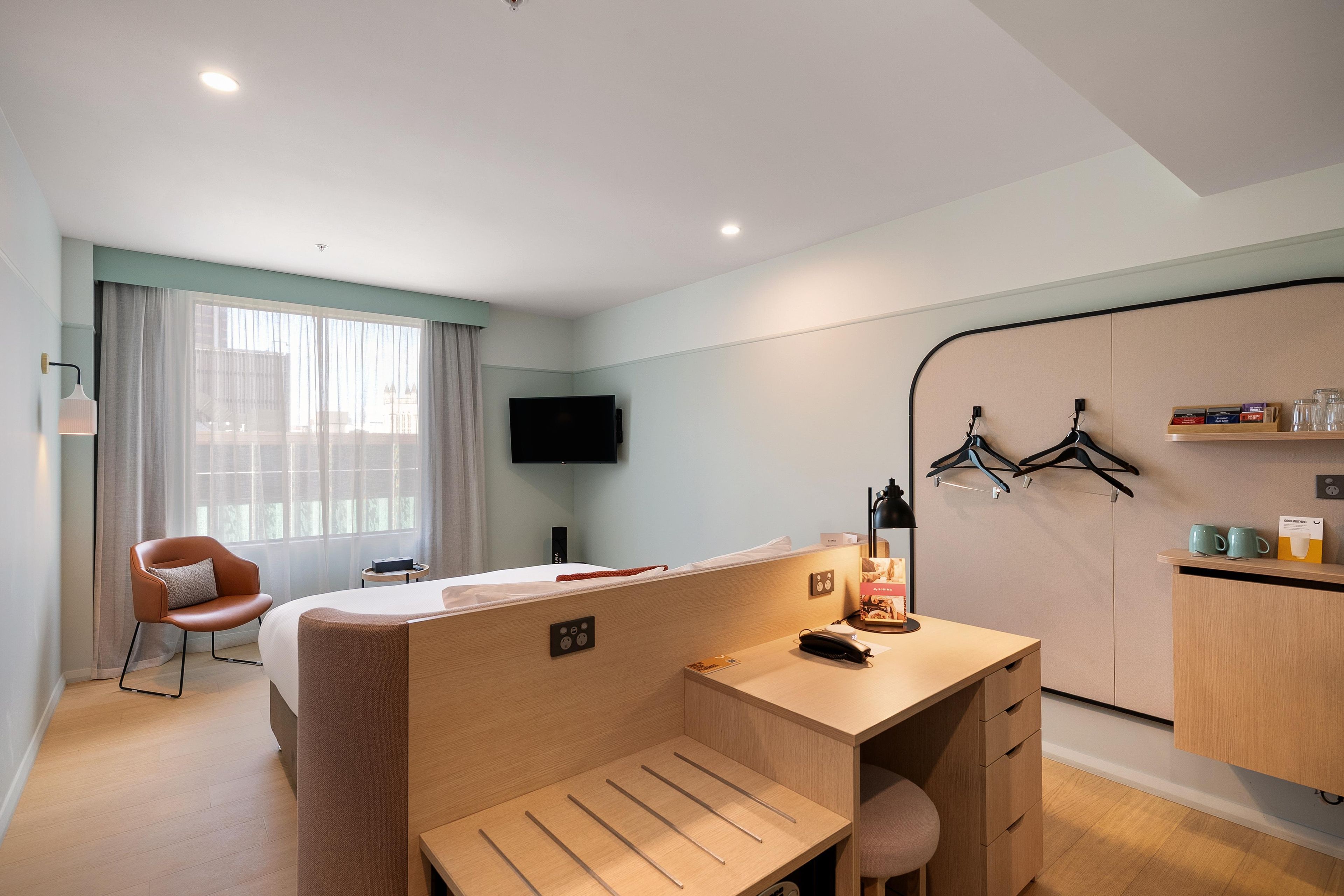 A hotel room with a single bed, a desk, a chair, a TV, and a wardrobe.