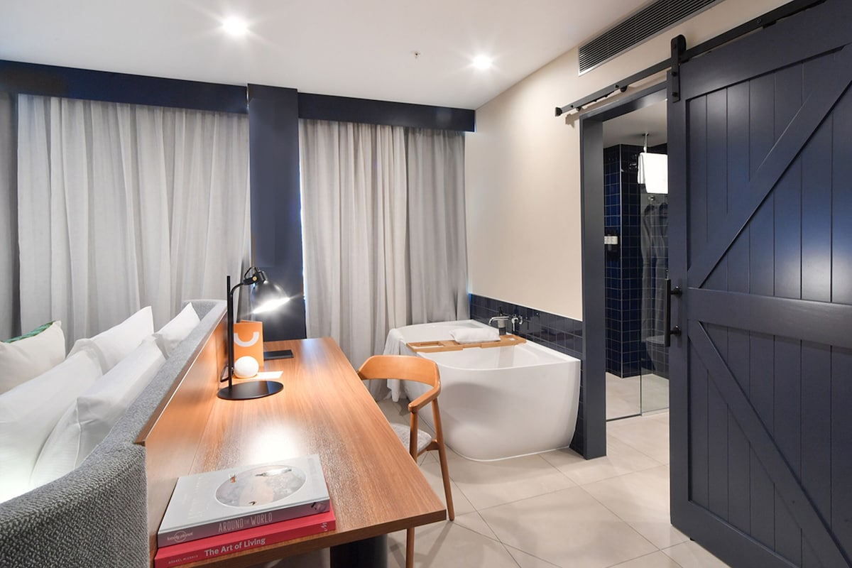 A modern bathroom with a bathtub, a wooden table, and a chair.