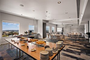 A spacious dining area with a long table set for a meal, large windows offering a view, and a modern interior design. - Sudima Auckland City (Auckland)