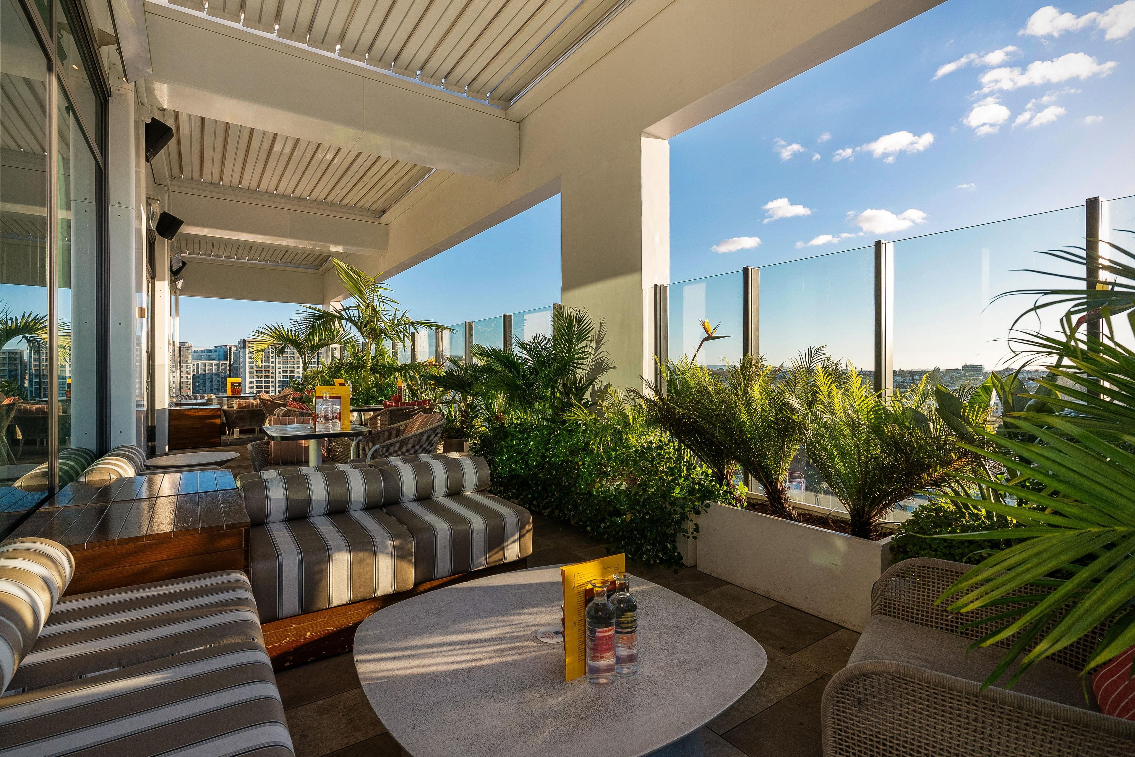 A rooftop terrace with outdoor seating, potted plants, and a clear view of the city skyline.