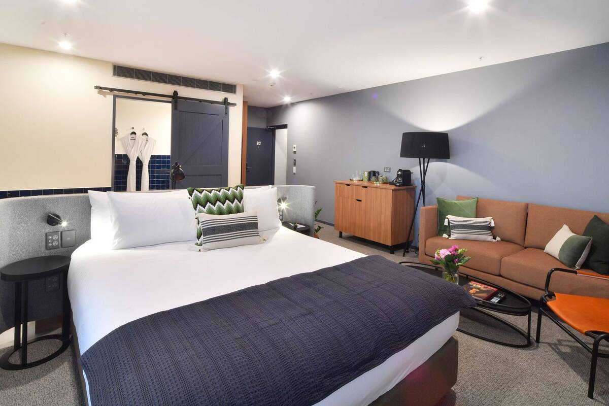 A modern hotel room with a large bed, a sofa, a coffee table, and a desk.