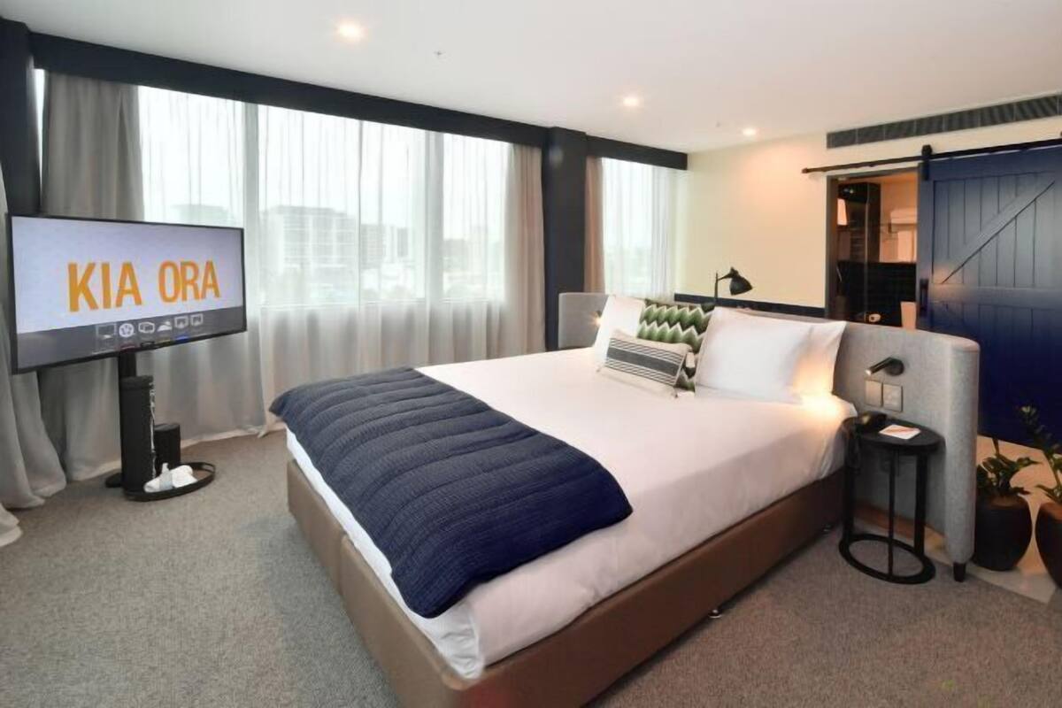 A hotel room with a bed, a TV, a desk, and a view of the city.