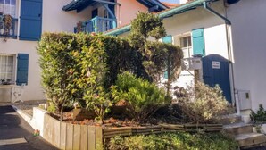 Um edifício residencial com persianas azuis, uma varanda e um jardim com diversas plantas.