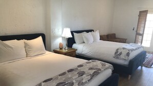 Une chambre d’hôtel avec deux lits, une table de chevet avec une lampe et une fenêtre avec des stores.