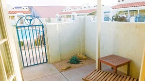 Un petit espace extérieur aménagé en patio, avec un banc en bois, une porte en métal et un sol en béton.