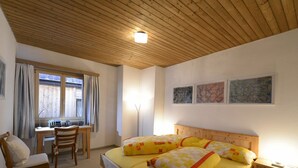 A bedroom with a wooden bed, a desk, and a chair. There are three framed pictures on the wall.