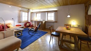 A cozy living room with a wooden ceiling, a dining area with a table and chairs, and a kitchen in the background.