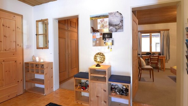 A room with wooden floors, a desk with a chair, a mirror, and a wall with various items and pictures.