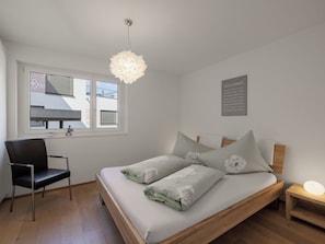 A bedroom with a bed, a chair, a bedside table, a wall-mounted light fixture, a window with blinds, and a motivational quote on the wall.