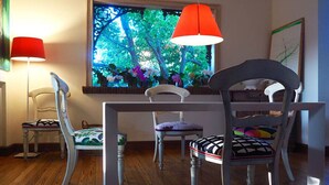 A dining area with a table and four chairs, a window with a view of trees, and a red pendant light. - Mondello Villa the two palm trees (Palermo)