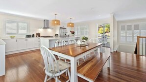 Een moderne keuken met witte kasten, een houten eettafel en hanglampen.