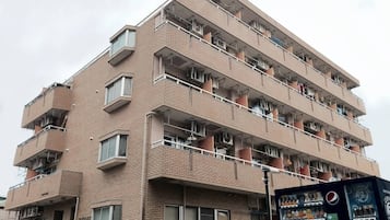A multi-story residential building with balconies, a vending machine, and a visible sign.