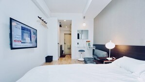 Quarto de hotel moderno, com uma cama grande, escrivaninha, cadeira e mesa de cabeceira com abajur.
