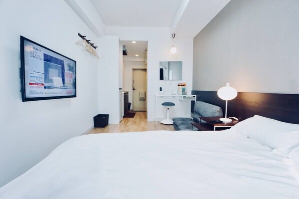 Ett modernt hotellrum med en stor säng, ett skrivbord, en stol och ett nattduksbord med en lampa.