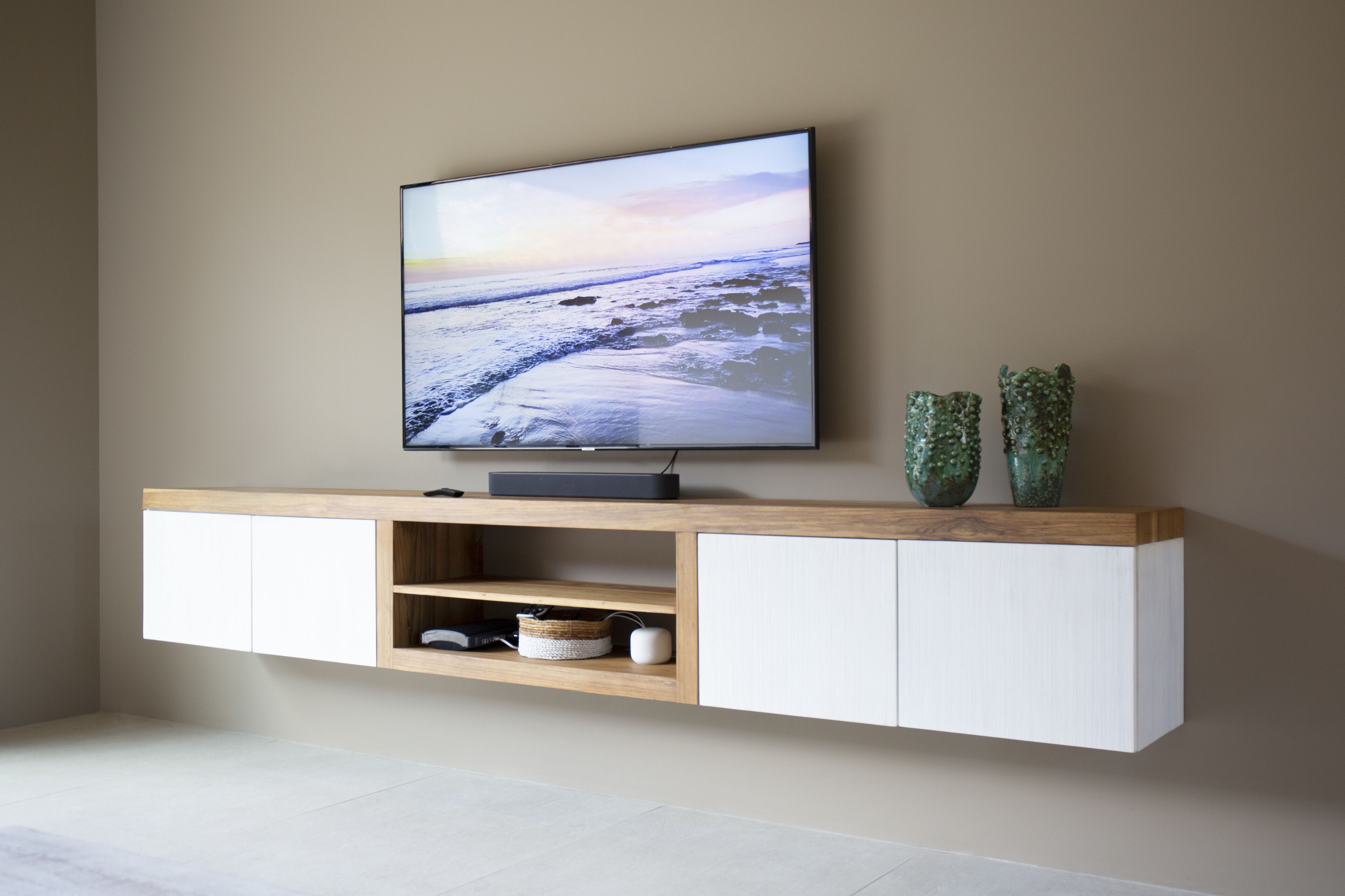 A flat-screen TV mounted on a wooden wall unit with two decorative vases.