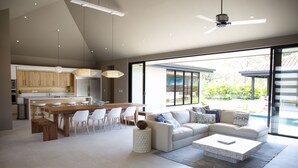A modern kitchen with a central island, white dining chairs, and a large window overlooking a garden.