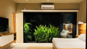 A modern bedroom with a bed, a TV, a large window, and a view of greenery.