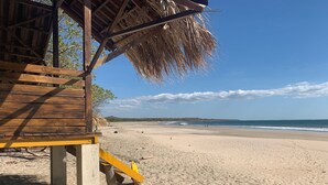 A wooden beach hut with a thatched roof, a sandy beach, and the ocean in the background.