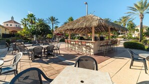 An outdoor patio area with tables and chairs, a thatched-roof bar area, and palm trees. - Ev7861ha - Regal Palms Resort & Spa - 4 Bed 3 Baths Townhouse (Davenport)