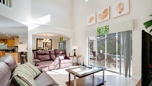 A spacious living room with a brown leather sofa, a glass coffee table, and a view of a balcony with outdoor furniture. - Ev8090ha - Providence - 4 Bed 3 Baths Villa (Davenport)