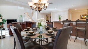 A dining area with a glass table, brown leather chairs, a chandelier, and a white floral centerpiece. - Ev8090ha - Providence - 4 Bed 3 Baths Villa (Davenport)