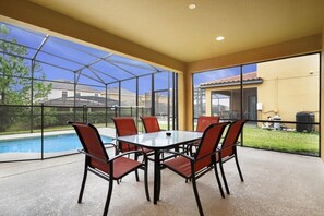 Eine überdachte Terrasse mit Glasveranda, Pool und Gartenmöbeln.