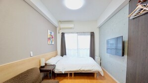 Een hotelkamer met een bed, een kleintje tafeltje, een stoel, een sofa, een airconditioner, een televisie en een raam met gordijnen.