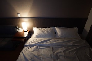 Restful retreat with a neatly made bed and a bedside table featuring a remote control and a charger.