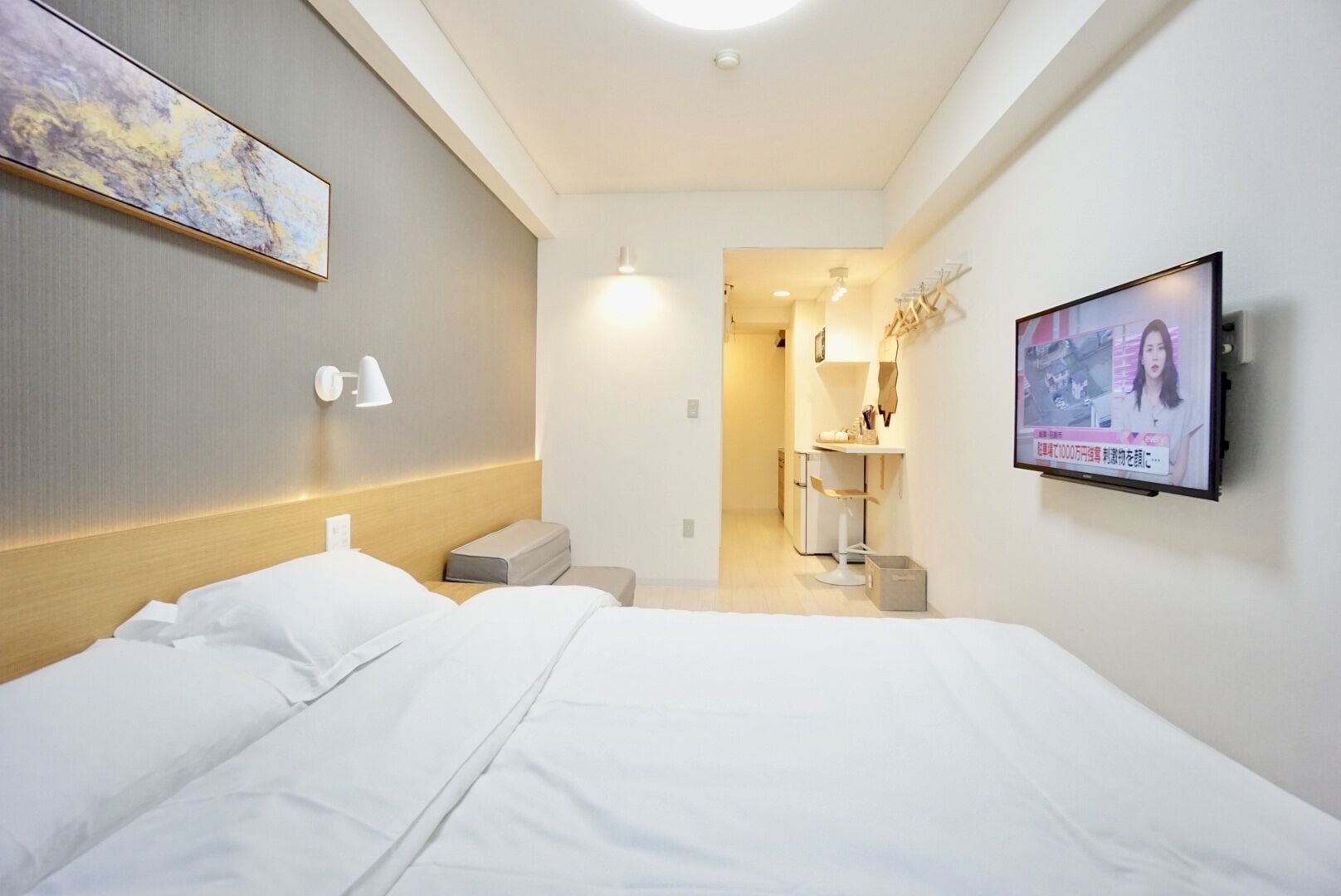 Ein Hotelzimmer mit Bett, Wandfernseher, kleinem Schreibtisch und einem durchgegangene Tür erkennbaren Badezimmer.