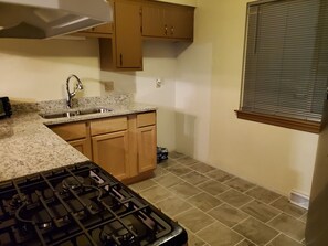 Una cocina con estufa a gas, encimera de granito, armarios de madera y una ventana con persianas.