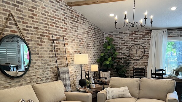 A living room with two beige sofas, a coffee table, a large mirror, a clock, and a chandelier.