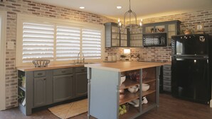 A kitchen with a brick wall, wooden countertop, and a black refrigerator.