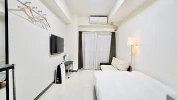 A hotel room with a bed, a desk with a chair, a TV, a wardrobe, and a window with curtains.
