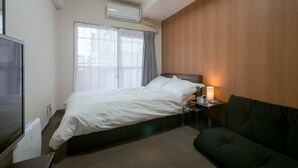 Ett hotellrum med en säng, ett nattduksbord med en lampa, en tv och ett fönster med gardiner.
