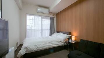 A hotel room with a bed, a bedside table with a lamp, a TV, and a window with curtains.