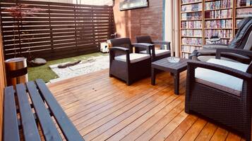 An outdoor patio area with wicker furniture, a small table, and a bookshelf filled with books.