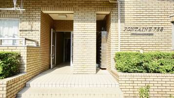 A building entrance with a brick facade, a sign reading "FONTAINE 758", and a small garden area with bushes.