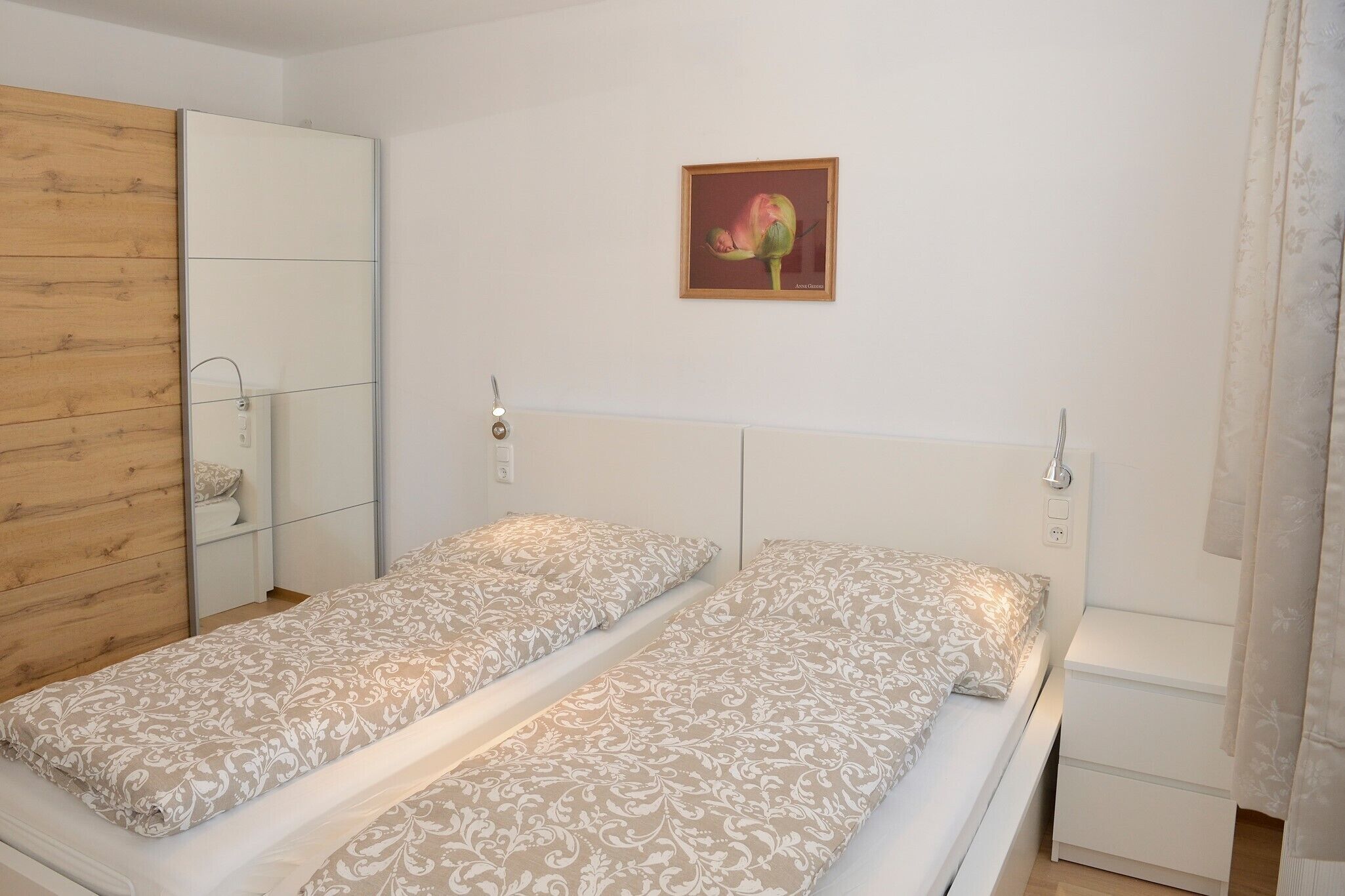 Une chambre à coucher avec une armoire en bois, un lit avec une literie à motifs, un miroir et un tableau encadré accroché au mur.