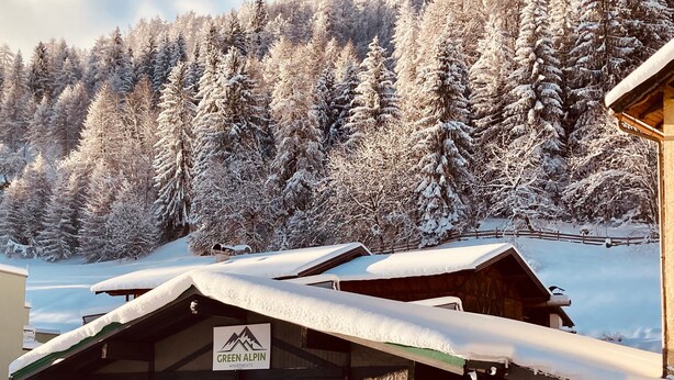 Ein schneebedecktes Gebäude mit einem Schild, auf dem 'Green Alpina Apartments' steht.